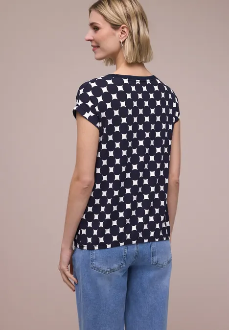 Person von hinten: kurzes blondes Haar, schwarzes T-Shirt mit weißem Sternmuster und blaue Jeans.